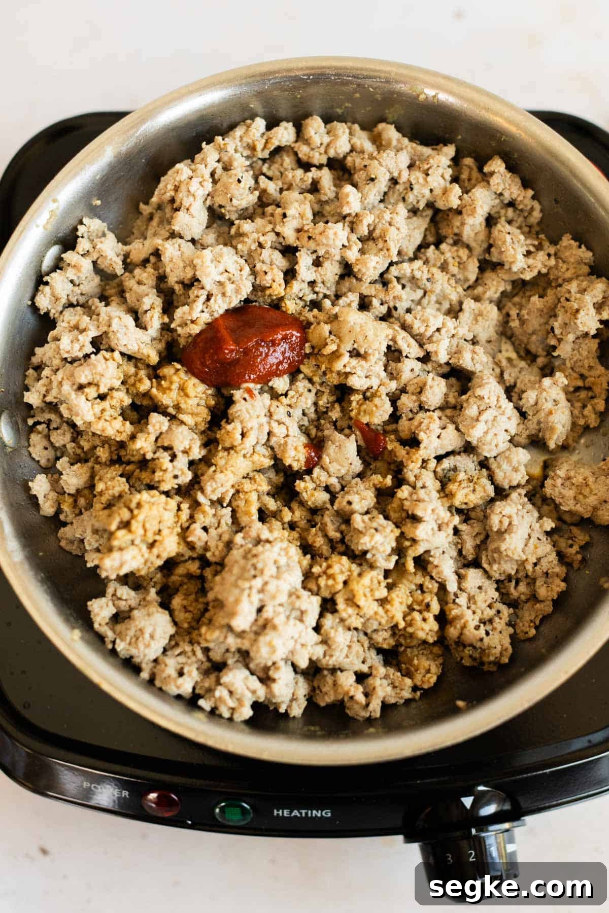 Ground Turkey Lettuce Wraps with Ginger-Soy Sauce 3 A pan of cooked ground turkey with a dollop of tomato paste and spices on a portable electric cooktop.