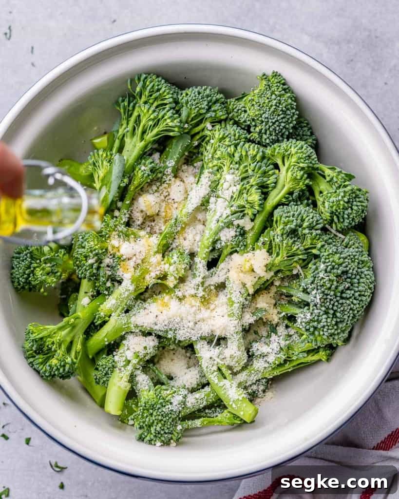 ingredients being added over raw broccolini in a bowl before roasting