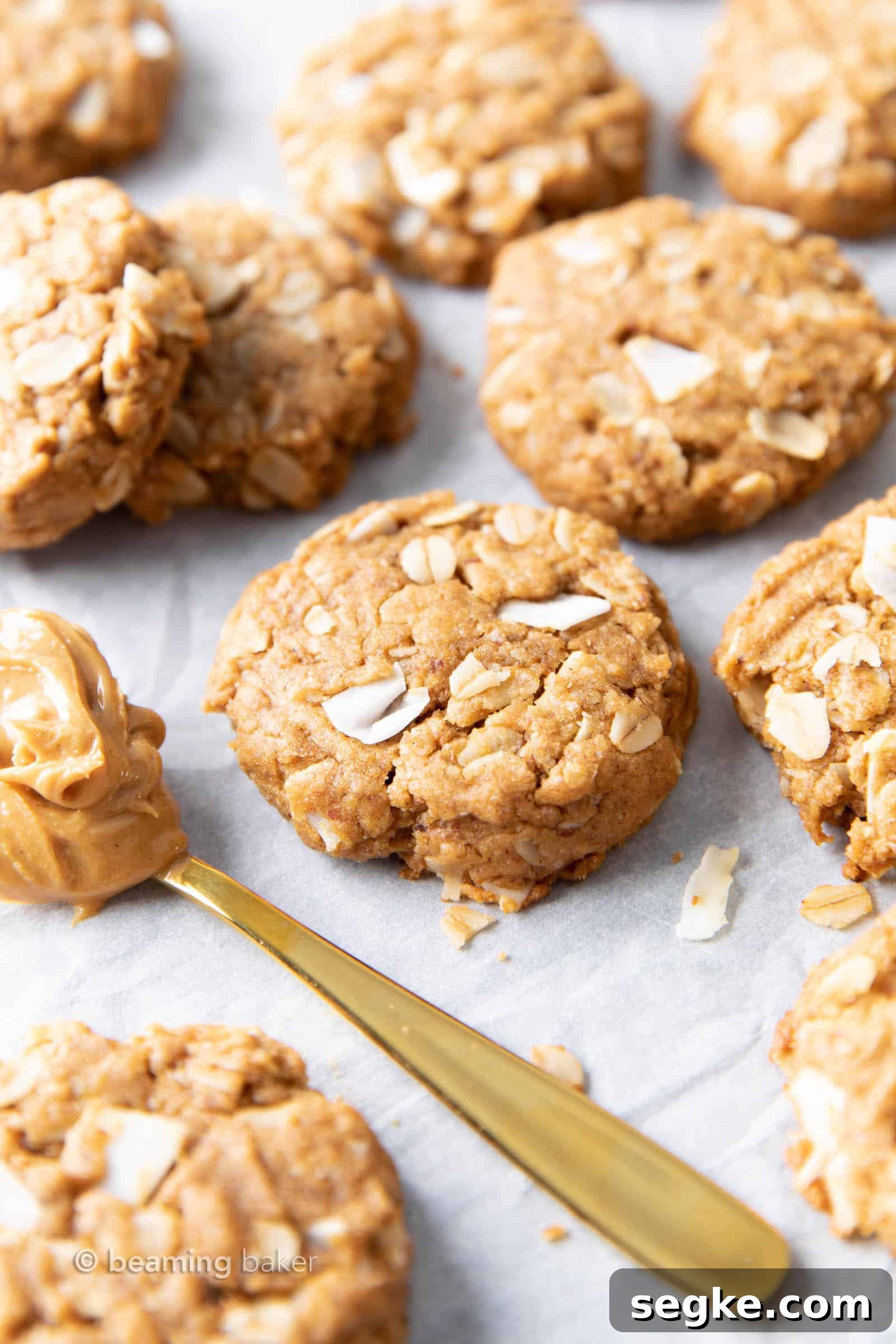 Several cookies on parchment paper with a gold spoon of peanut butter to it's left.
