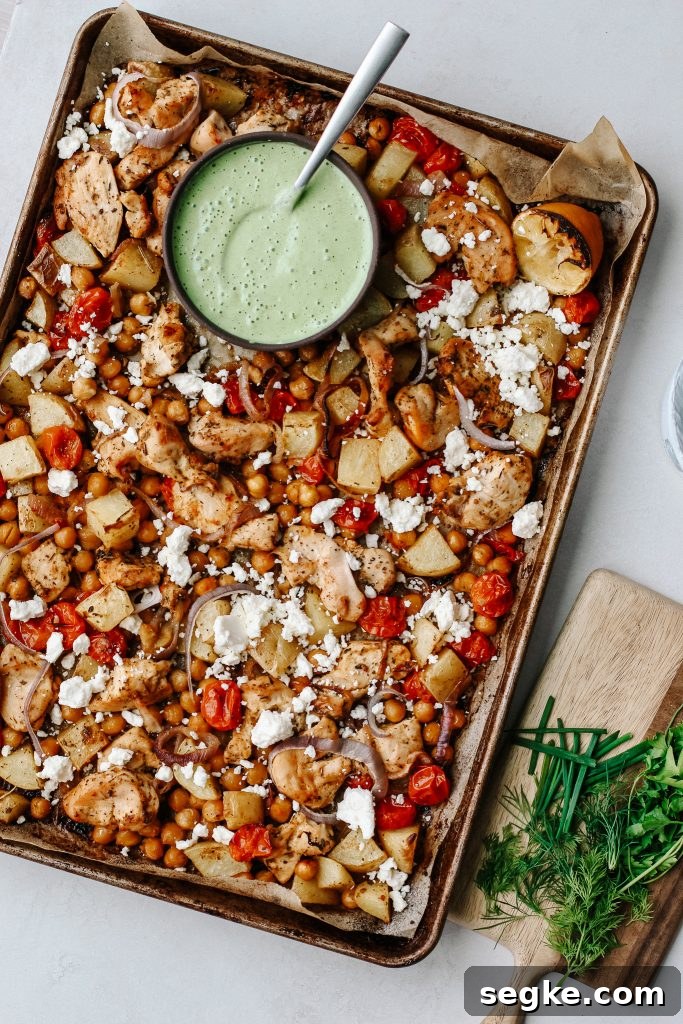 chicken and veggies on sheet pan with green yogurt sauce with herbs on wood cutting board