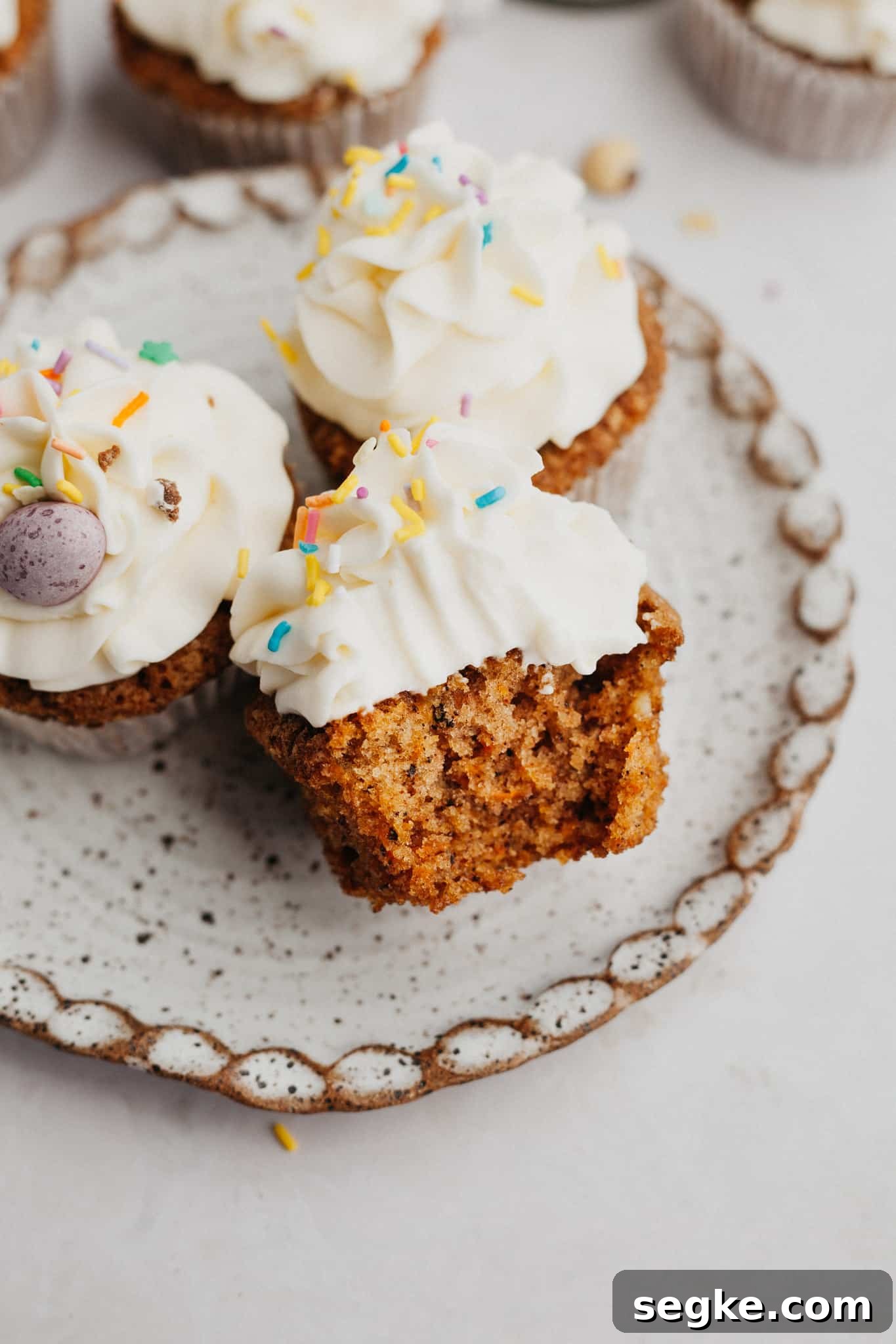A small plate with three carrot cupcakes, one has a bite taken out of it.