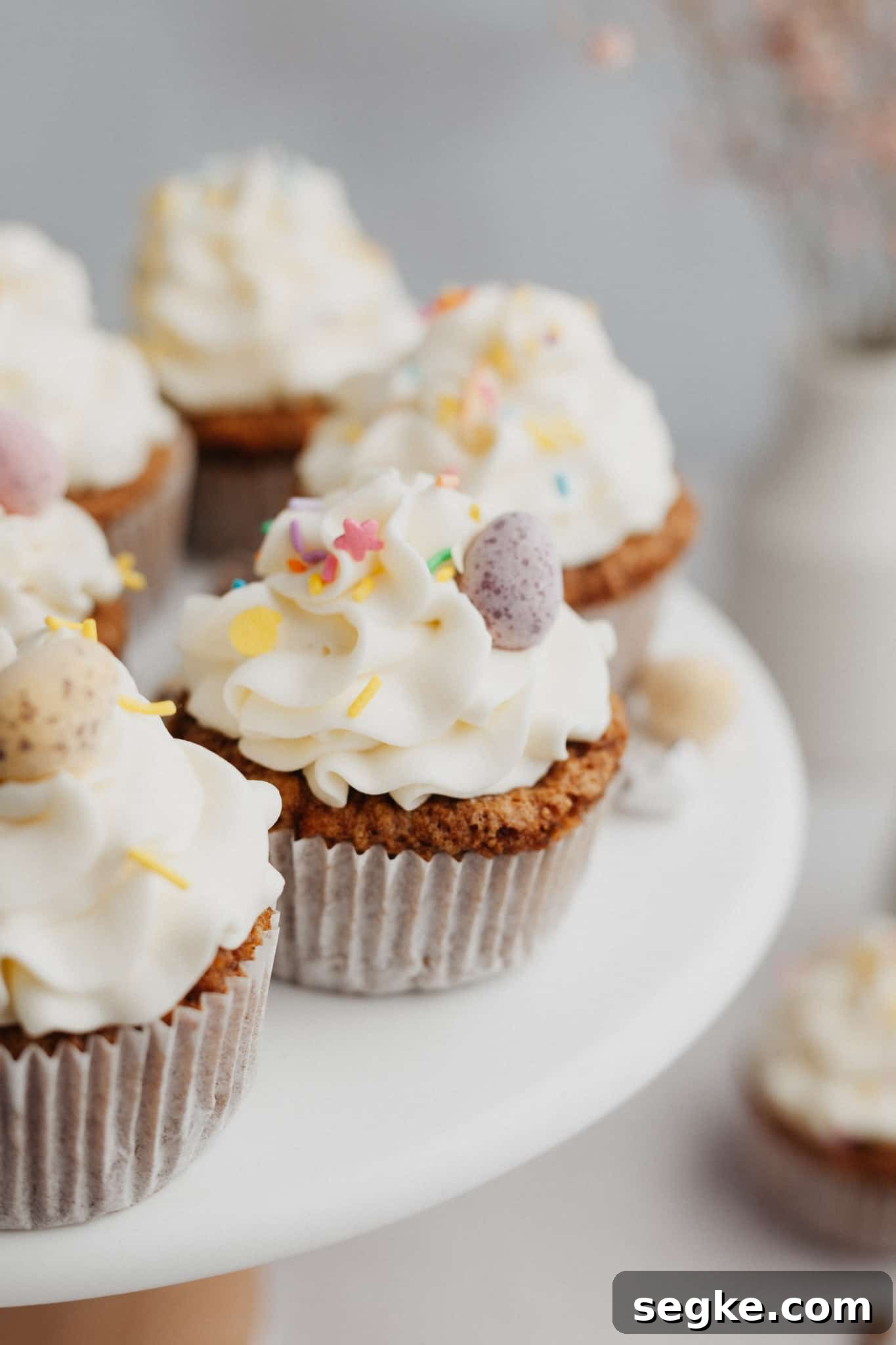 Several carrot cupcakes with white frosting on a cake stand.