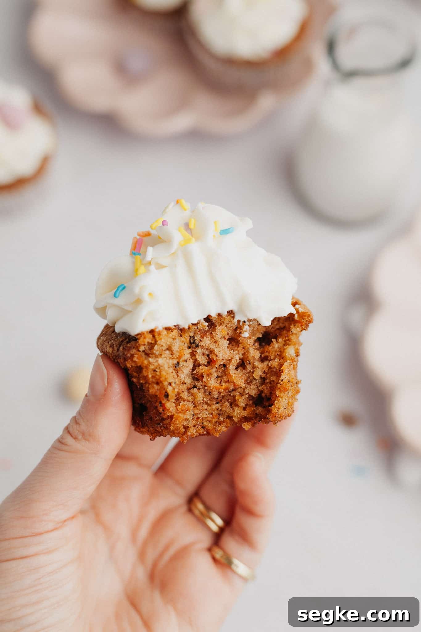 A hand holding a carrot cupcake with a bite taken out of it.