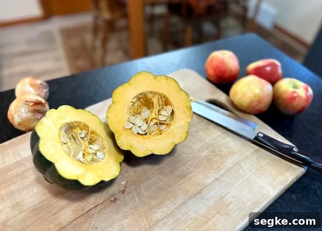 Acorn squash cut in half with seeds exposed beside apples and knife on cutting board — prepping vegetables for roasting.