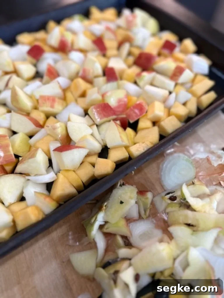 Cubed acorn squash, apples, and onions tossed on a sheet pan with olive oil before roasting — easy vegetable medley.