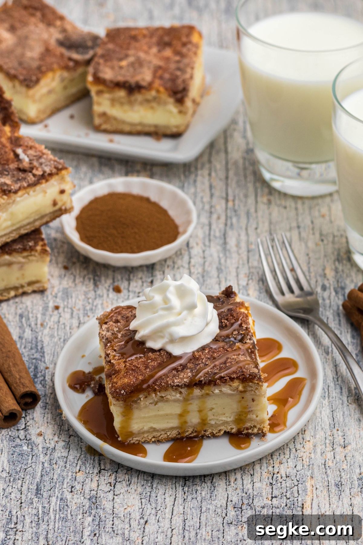 Cinnamon Churro Cheesecake with Crunchy Sugar Crust 2 Slice of cheesecake on a small white plate, drizzled with caramel syrup and topped with whipped cream.