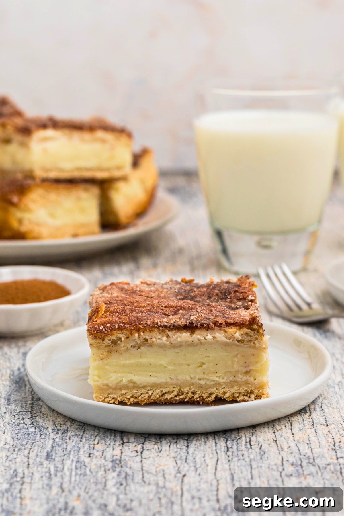 Cinnamon Churro Cheesecake with Crunchy Sugar Crust 5 Slice of churro cheesecake served on a small white plate in front of glasses of milk.