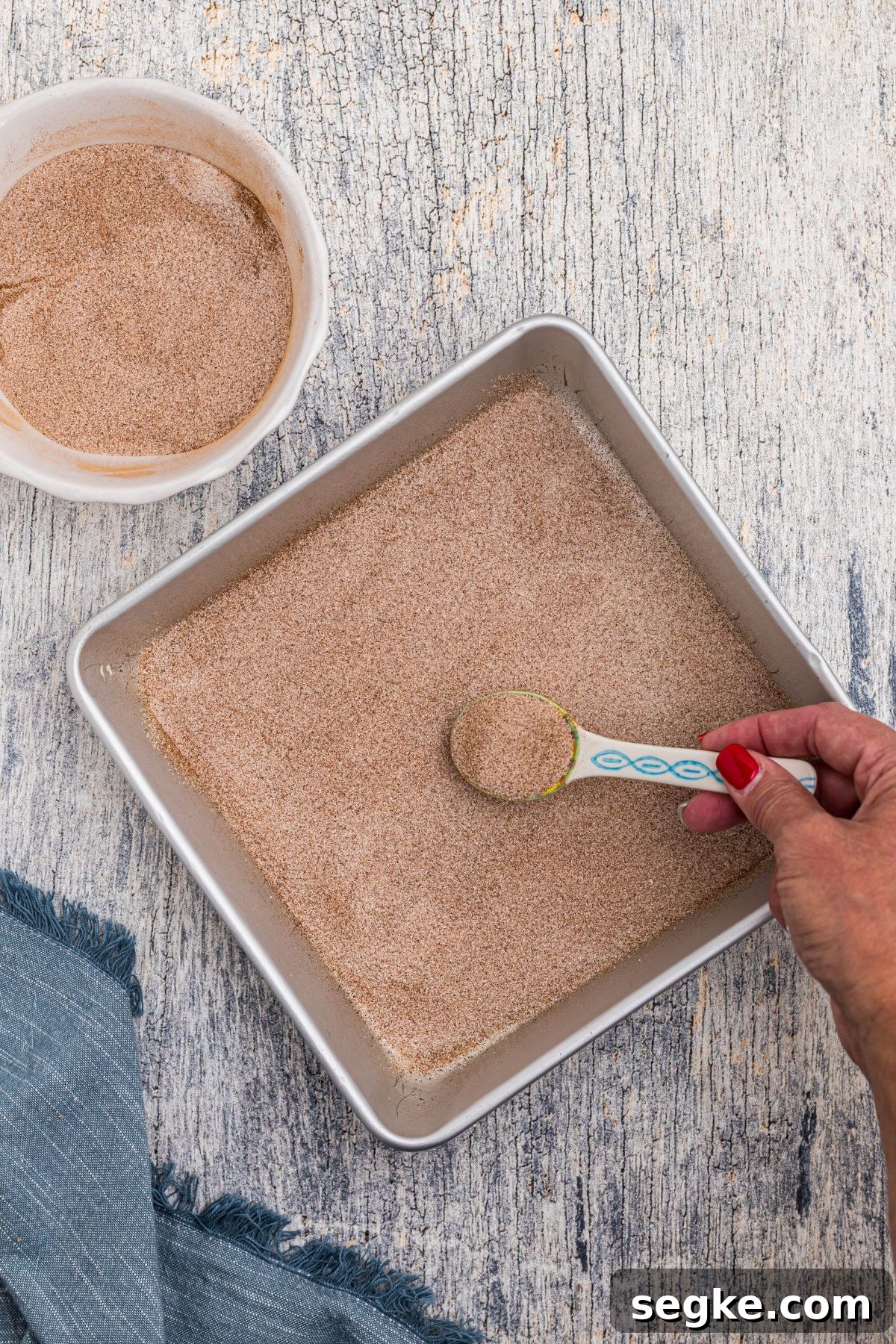 Cinnamon Churro Cheesecake with Crunchy Sugar Crust 4 Sugar and cinnamon mixture being added to bottom of square pan.