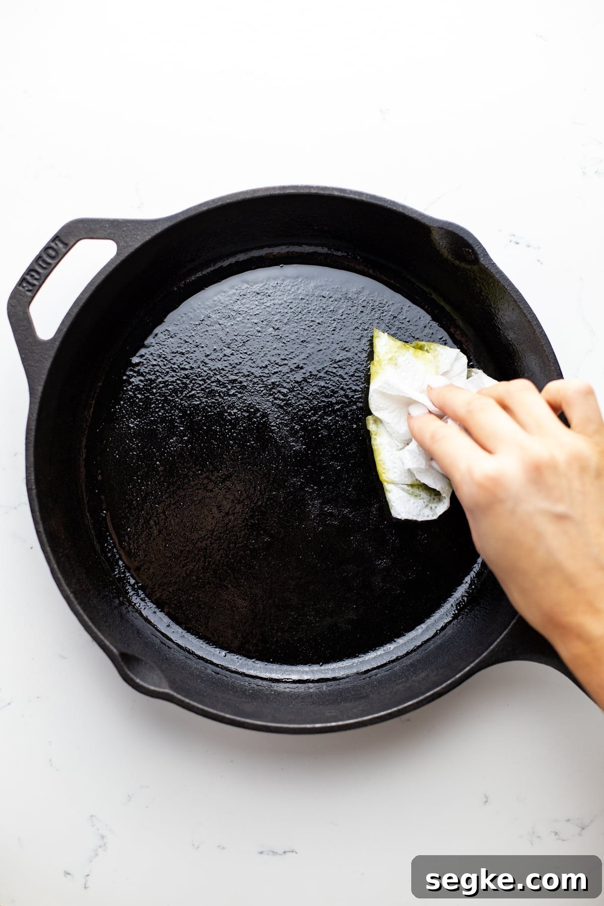How to Make Crispy Cast Iron Skillet Pizza 2 A hand using a paper towel to wipe oil in a black cast iron pan.