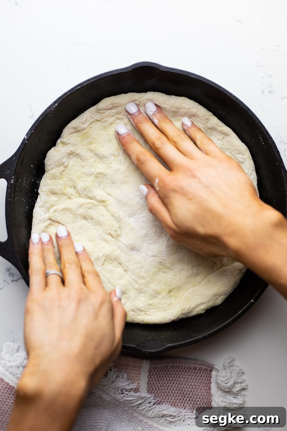How to Make Crispy Cast Iron Skillet Pizza 4 Hands stretch pizza dough out in a black cast iron skillet.