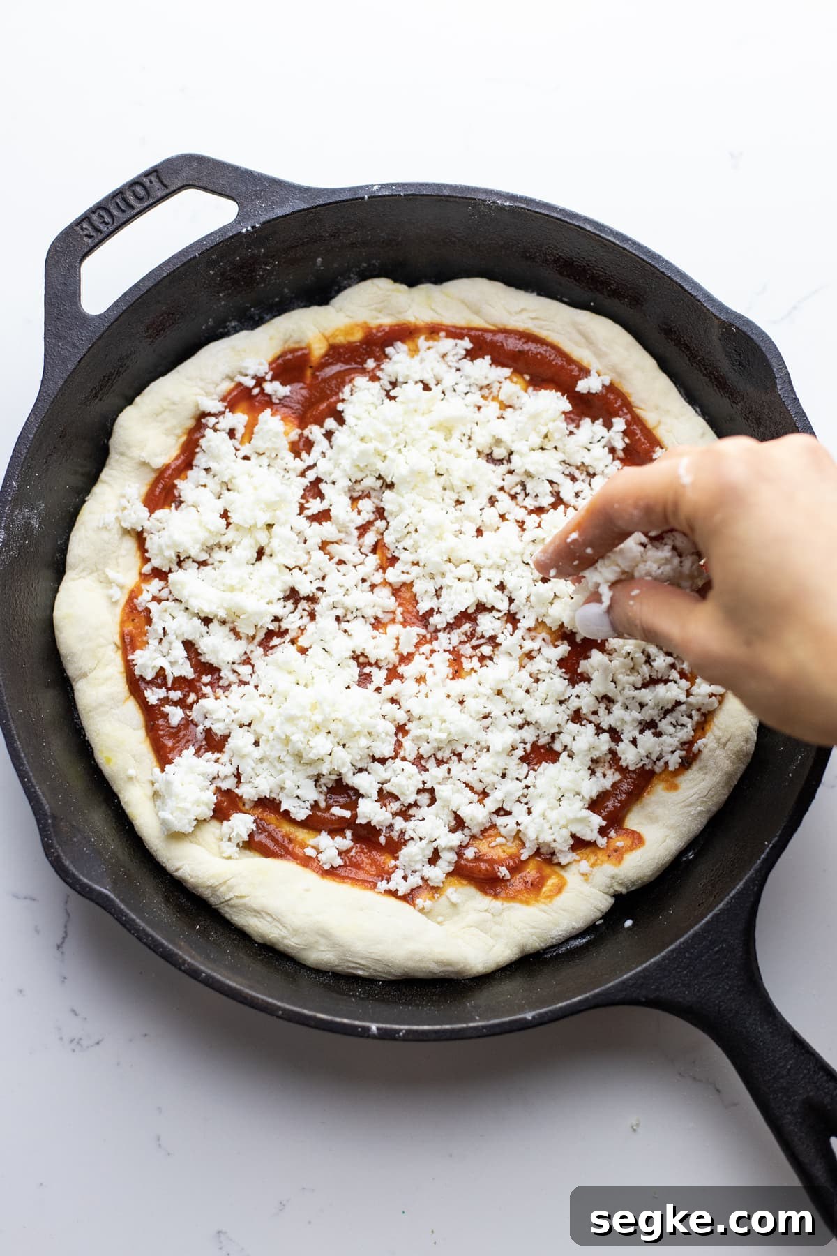 How to Make Crispy Cast Iron Skillet Pizza 6 A hand sprinkling cheese over a cast iron skillet pizza.