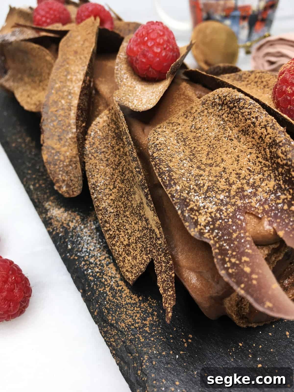 Chocolate raspberry roll cake on a slate board; a cup and berries in the background