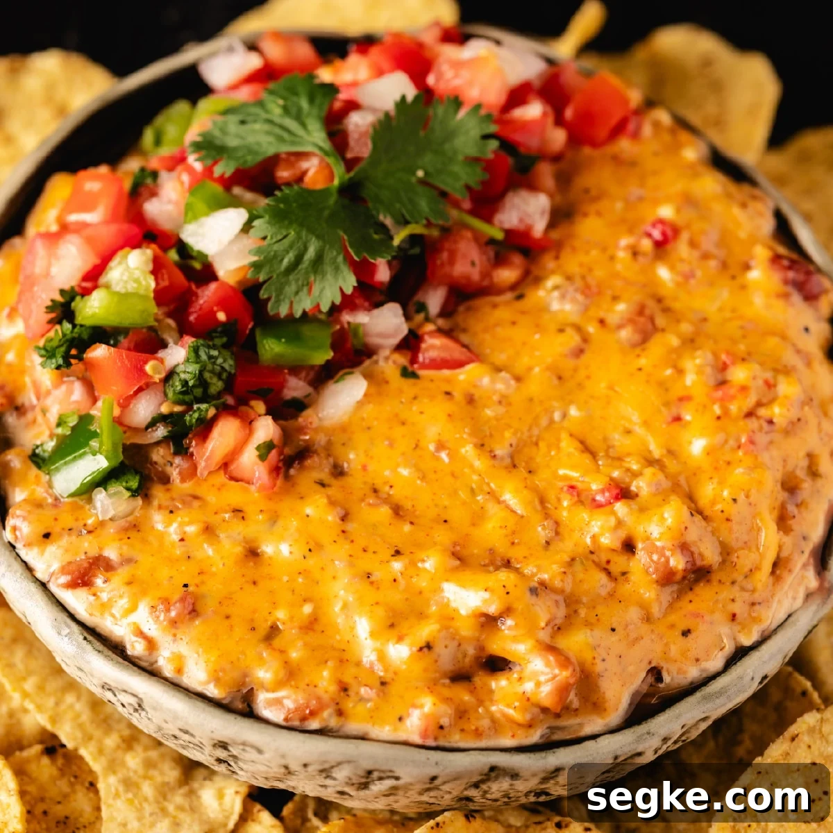 5 Game Day Dip Recipes Your Guests Will Love 3 A bowl of smoked queso topped with fresh pico de gallo sitting on a bed of tortilla chips.