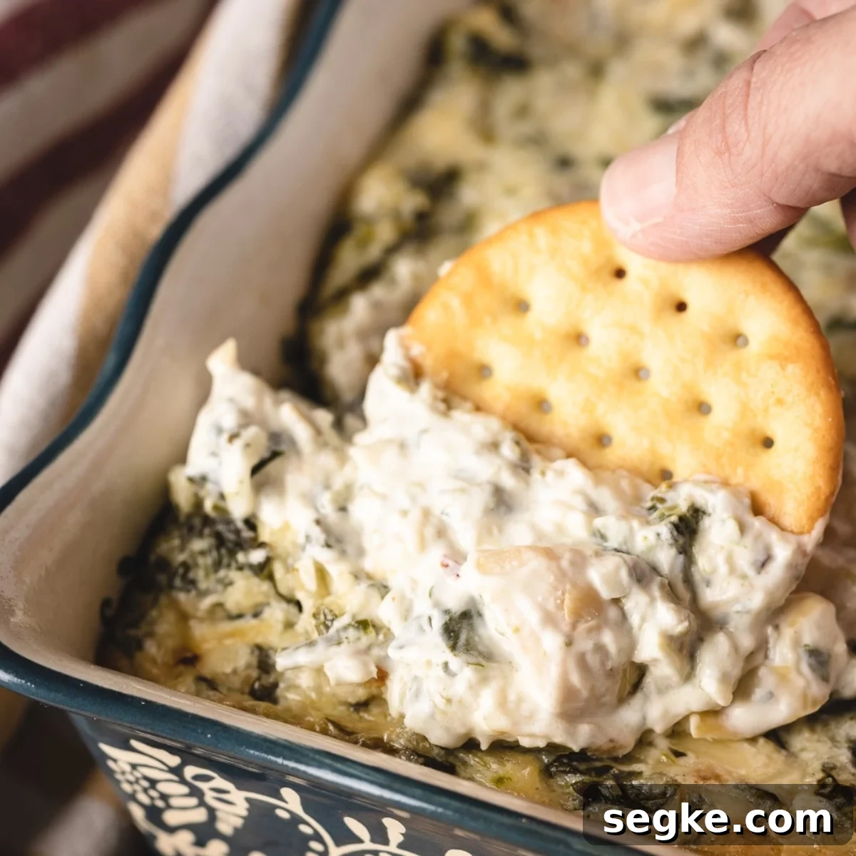 5 Game Day Dip Recipes Your Guests Will Love 4 A hand pulling a cracker from a game day spinach and artichoke dip.