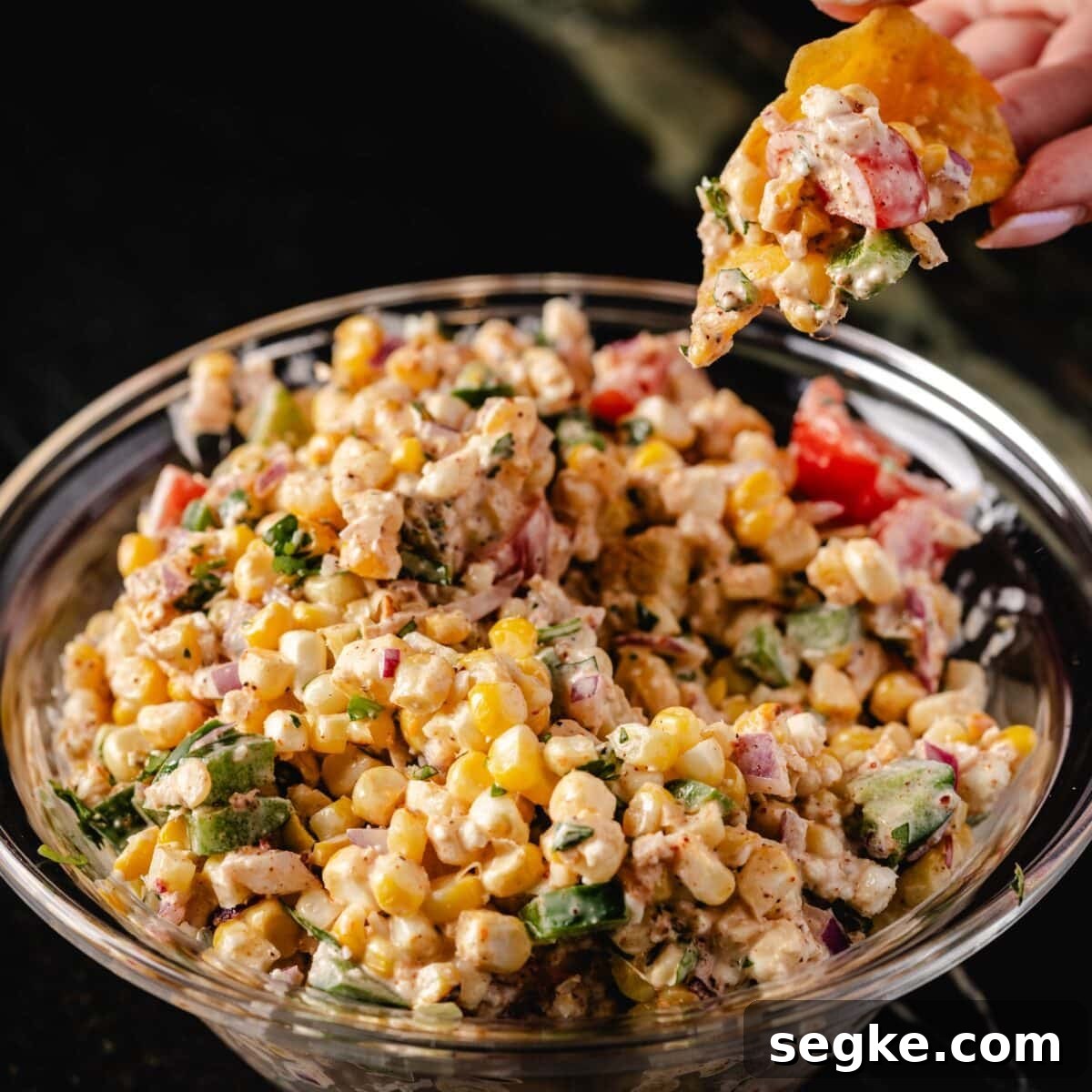 5 Game Day Dip Recipes Your Guests Will Love 5 A large glass bowl full of corn salsa, and a hand holding a chip with a scoop of the salsa above the bowl.