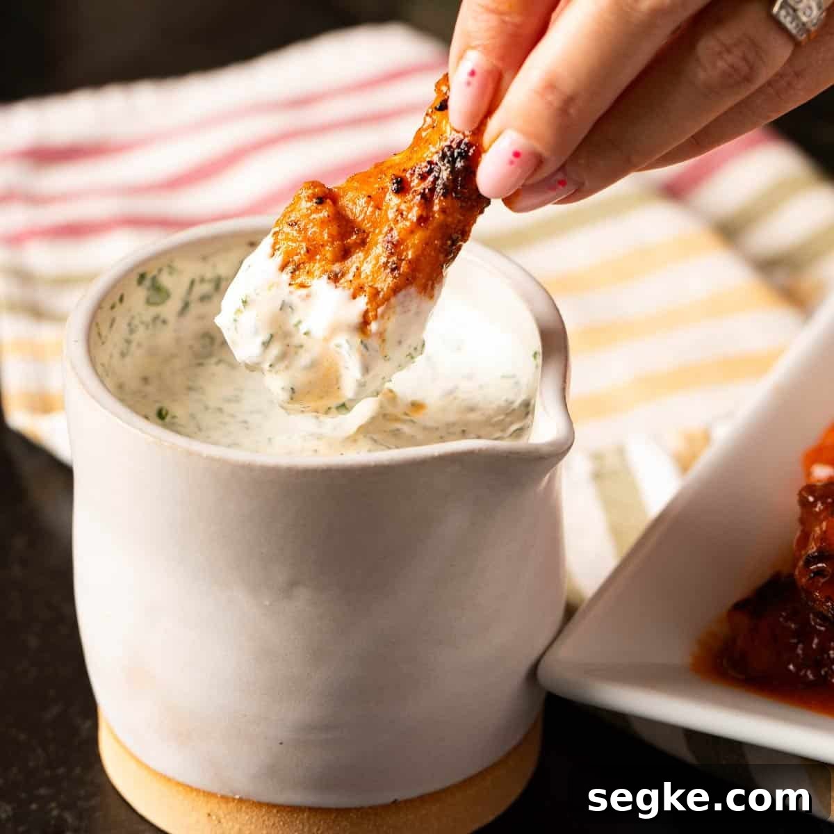 5 Game Day Dip Recipes Your Guests Will Love 6 Buffalo wing being dipped into jar of dipping sauce.