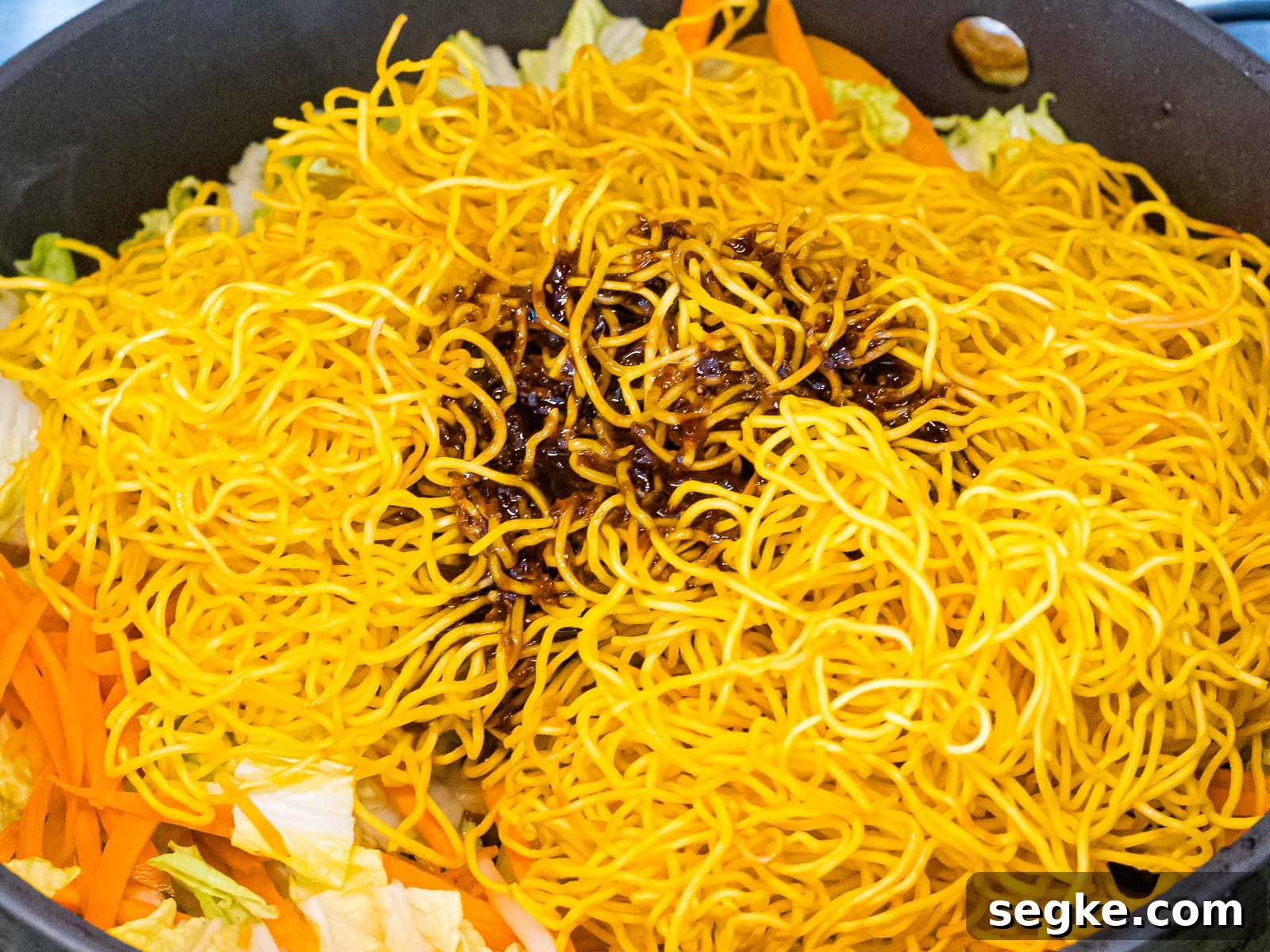 chow mein noodles with sauce added to a pan with vegetables