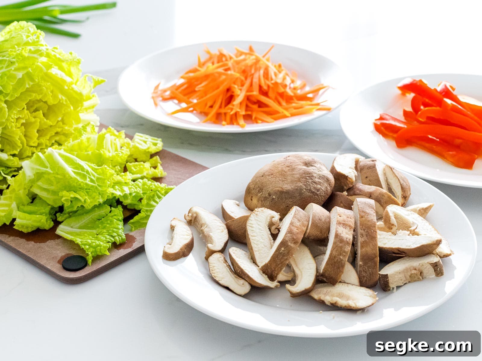 sliced shiitake mushrooms, chopped cabbage, julienned carrots and red peppers on white plates