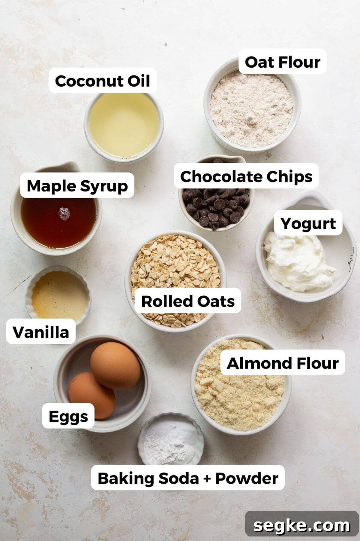 Ingredients for healthy chocolate chip oatmeal muffins including rolled oats, almond flour, Greek yogurt, maple syrup, and chocolate chips.