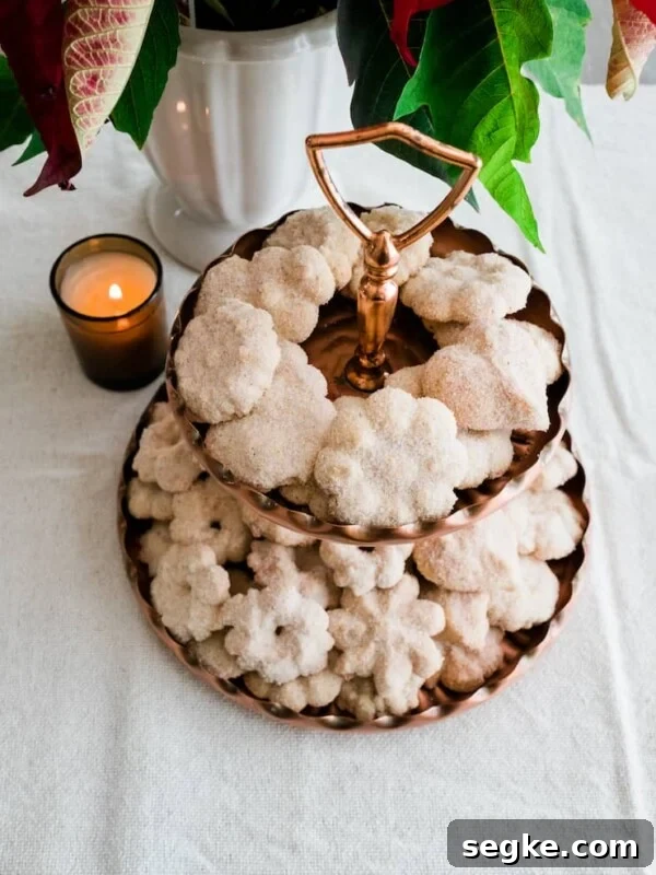 Biscochos, traditional Mexican wedding cookies, displayed on a brass dessert stand with a poinsettia and candle in the background.