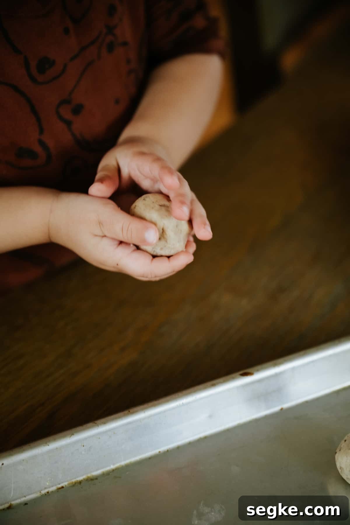 child's hands rolling a piece of polvoron dough into a ball.