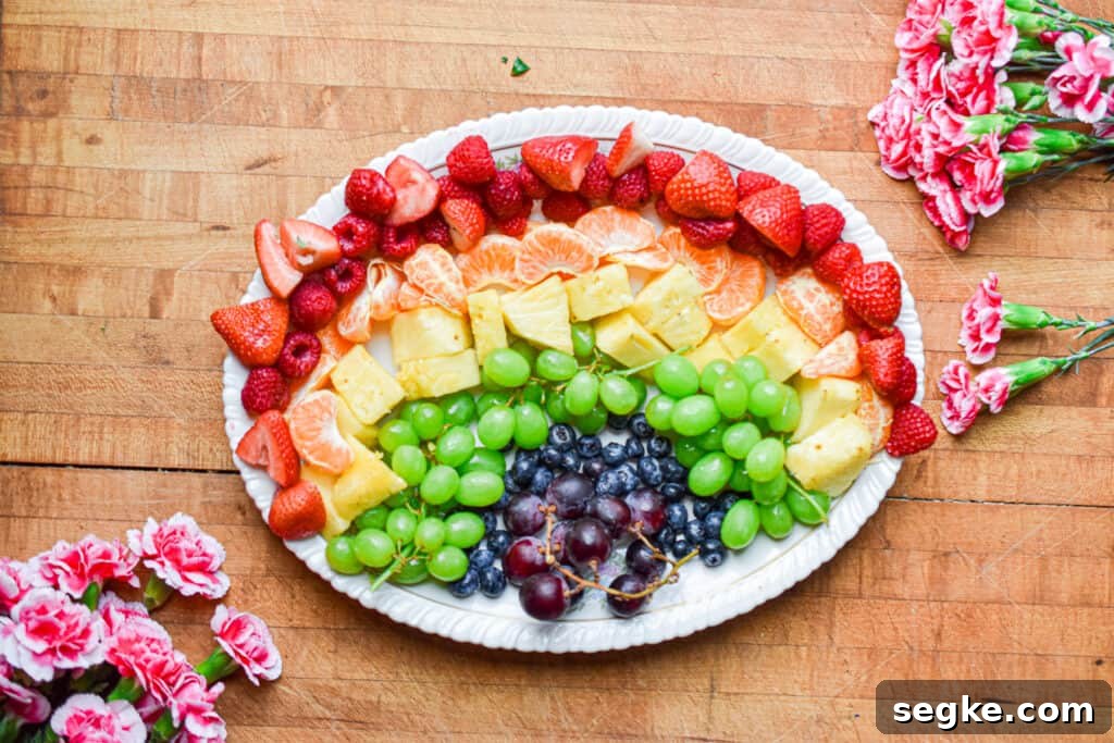 Flowers are surrounding the platter with the rainbow fruit on it.