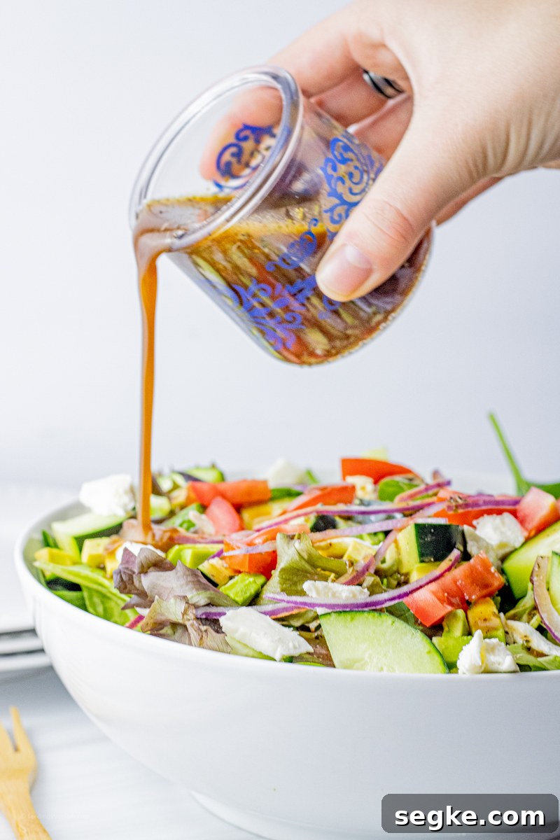 hand pouring balsamic vinaigrette over a green salad in a white bowl