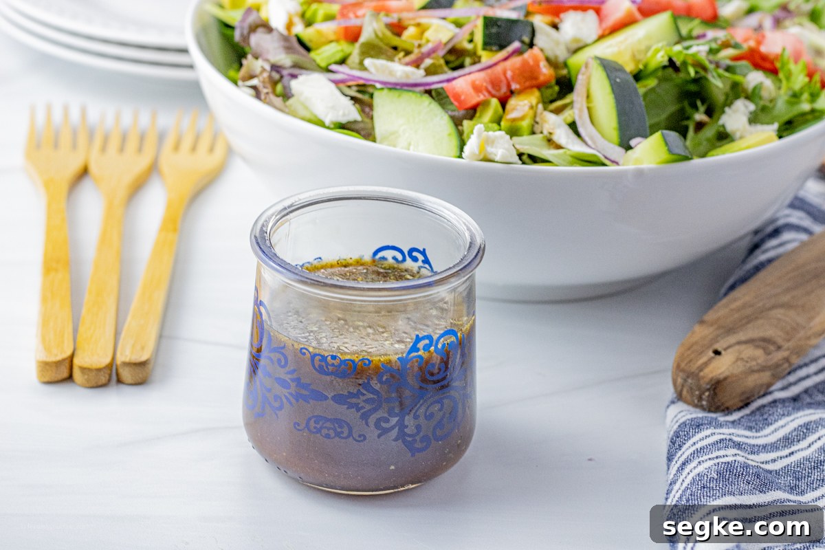 small glass jar with balsamic vinegar dressing in it in front of a large white bowl filled with green salad