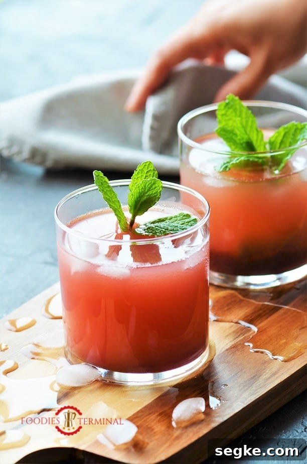 Gorgeous pink Kokum Sharbat in two glasses on a wood board with broken ice cubes all around