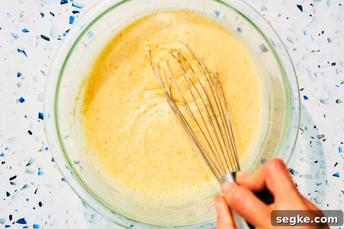 Mini cornbread muffin batter being whisked in a glass bowl.