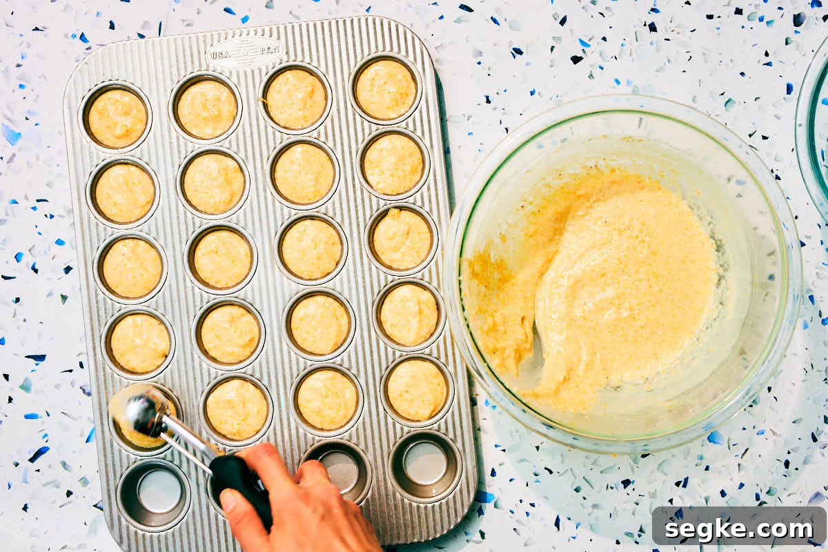 Cornbread batter being scooped into mini muffin tins.