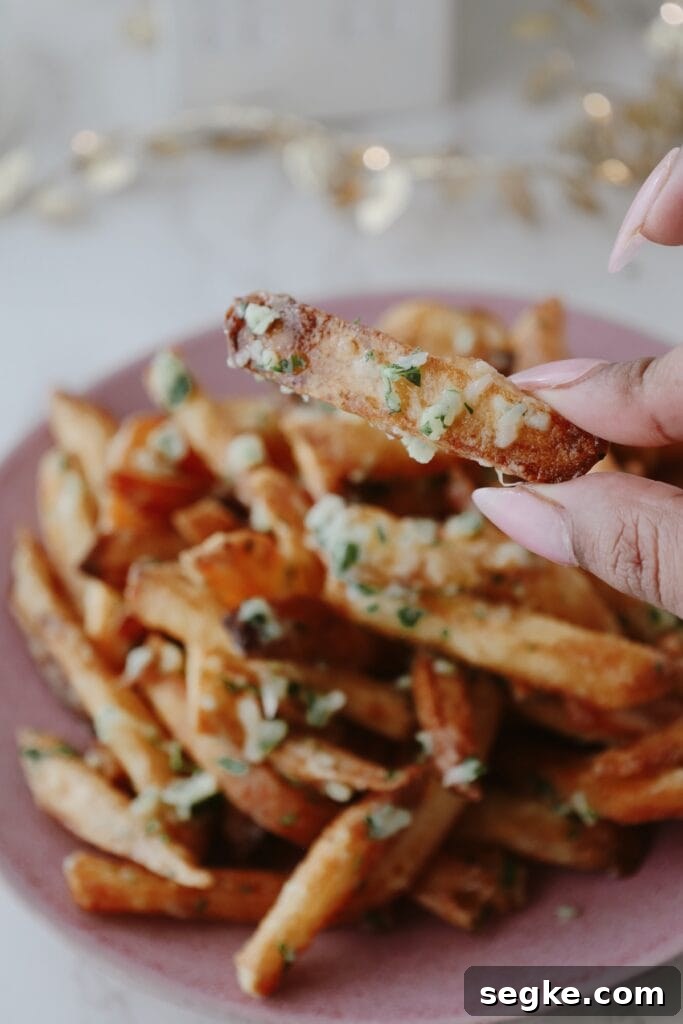 Crispy Truffle Fries with Parmesan 3 a hand holding one of the truffle french fries
