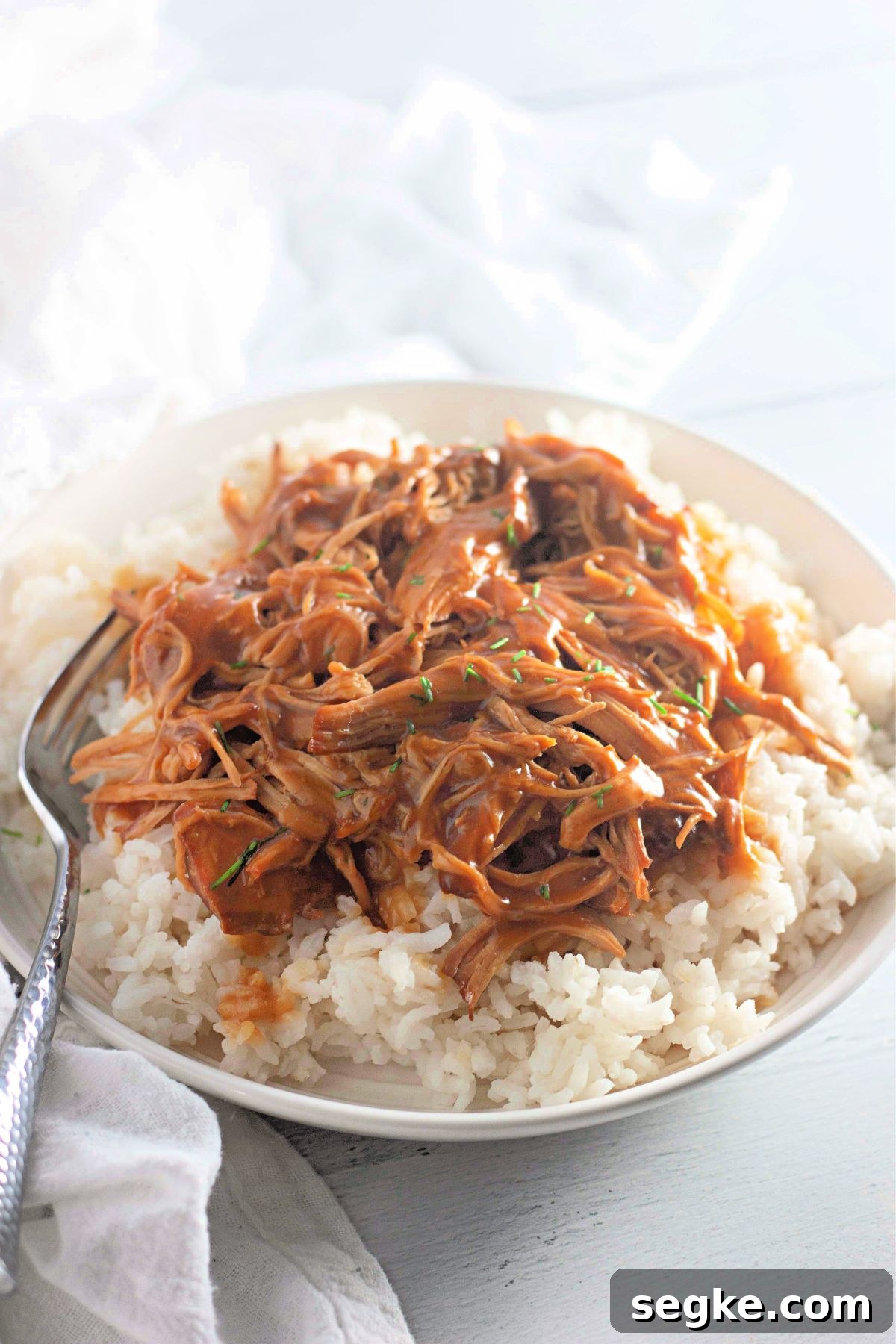 5-Ingredient Paleo Slow Cooker Chicken Recipe 2 Paleo honey garlic chicken shredded on white rice in a bowl with a fork in the bowl.