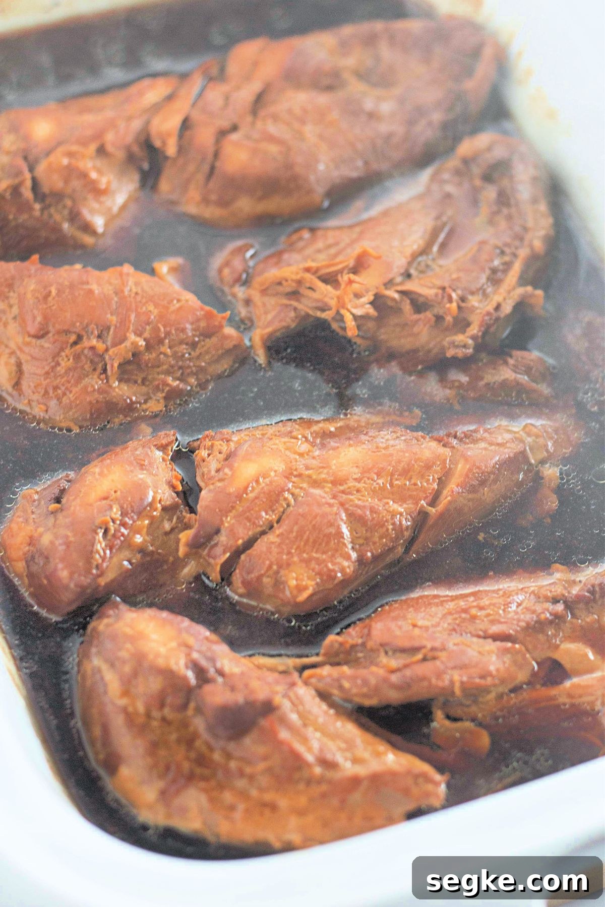 5-Ingredient Paleo Slow Cooker Chicken Recipe 5 Chicken breasts cooking in honey garlic sauce in a white slow cooker.