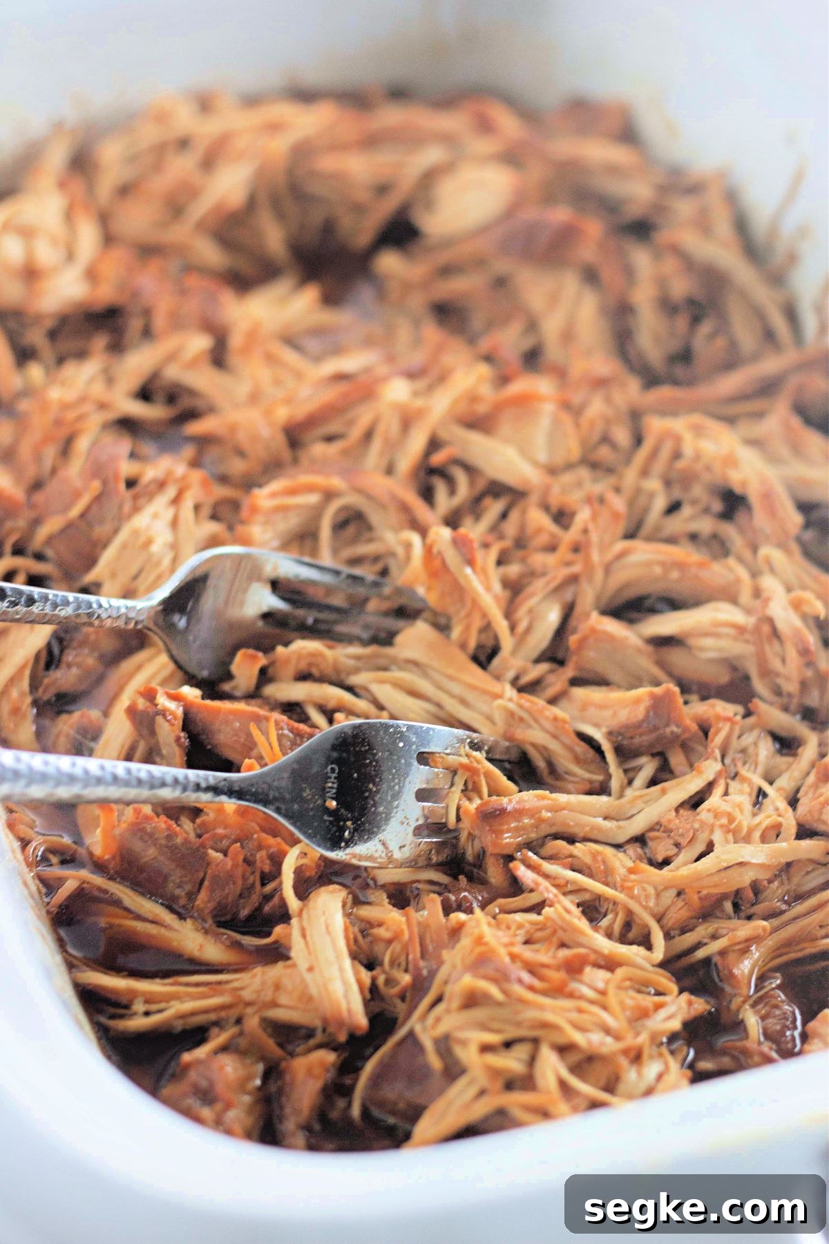 5-Ingredient Paleo Slow Cooker Chicken Recipe 6 Two forks shredding honey garlic chicken in a white slow cooker.