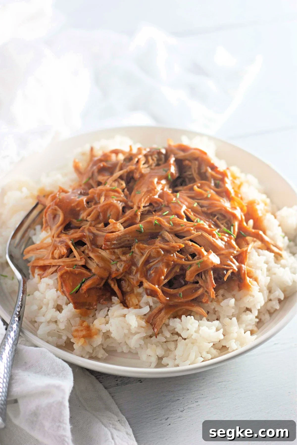 5-Ingredient Paleo Slow Cooker Chicken Recipe 7 Paleo honey garlic chicken shredded on white rice in a bowl with a fork in the bowl.