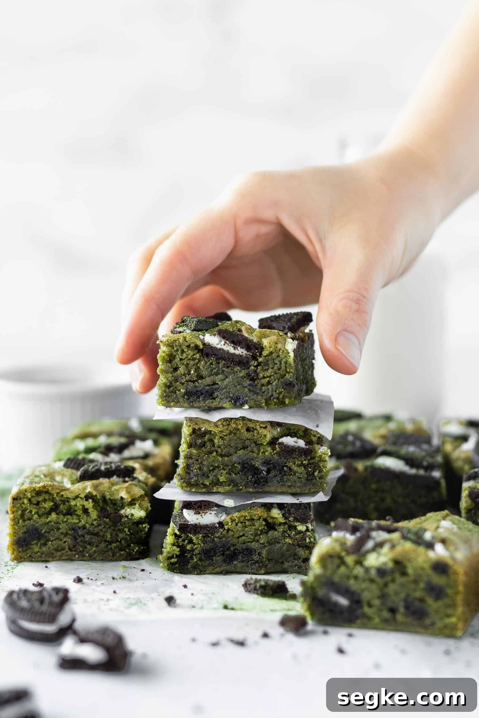 A hand reaching for a stack of matcha blondies