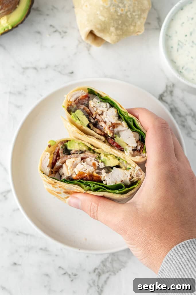 A hand holding the wrap cut in half on a white plate.