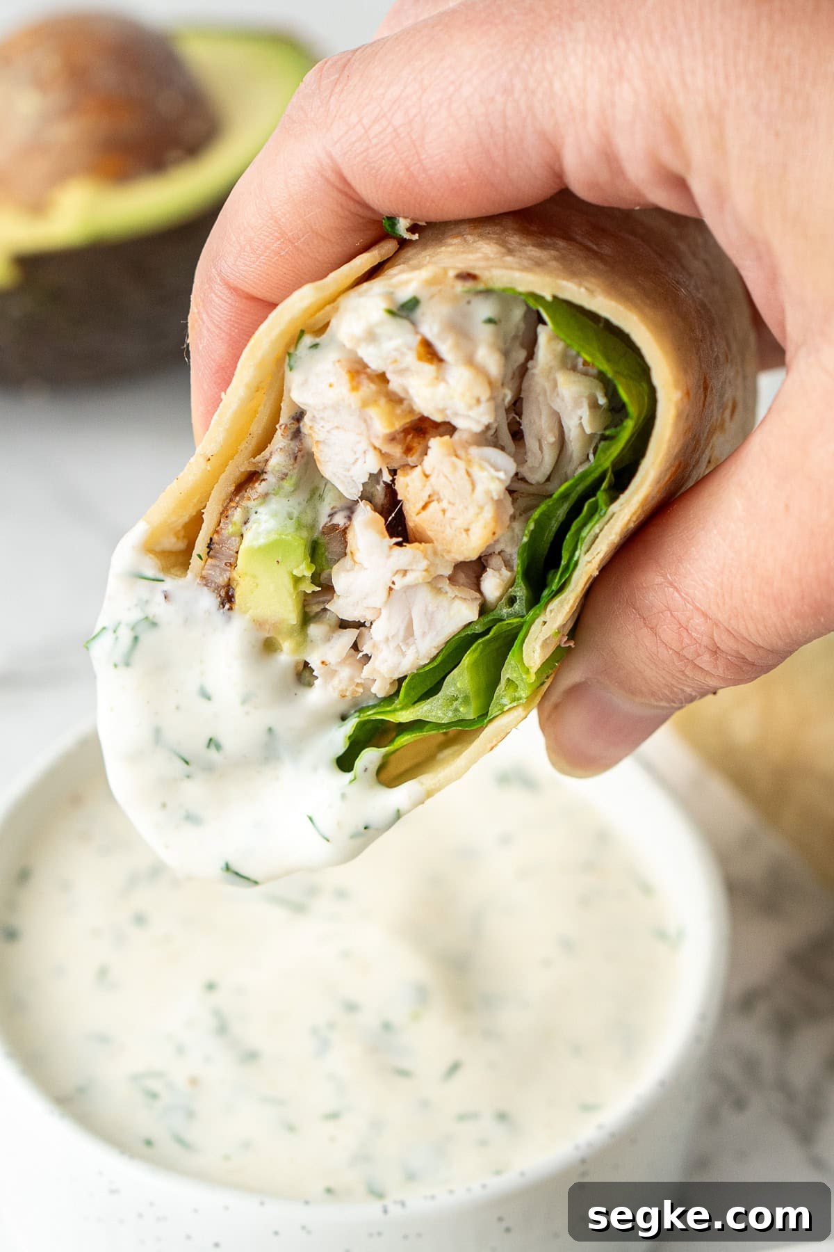 A hand holding half of a chicken bacon wrap dunking it in ranch. 