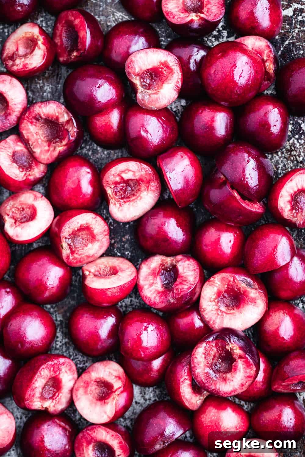 Overhead close-up of halved and pitted fresh dark red cherries on a dark baking sheet before roasting.