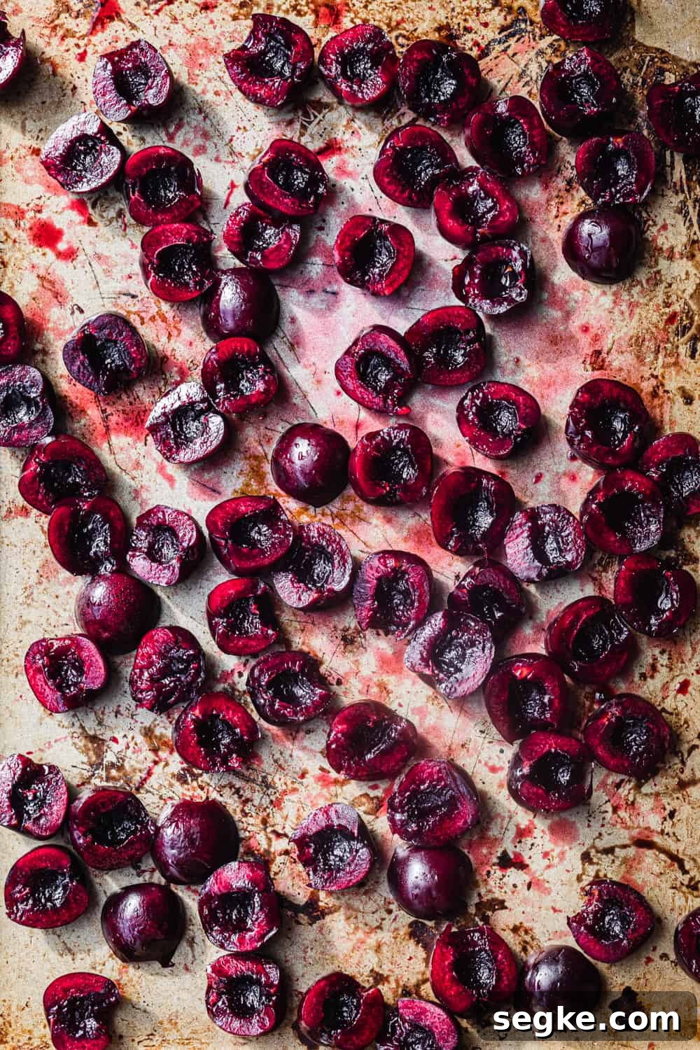 Raw fresh cherries cut in half on a gold baking sheet, overhead shot.