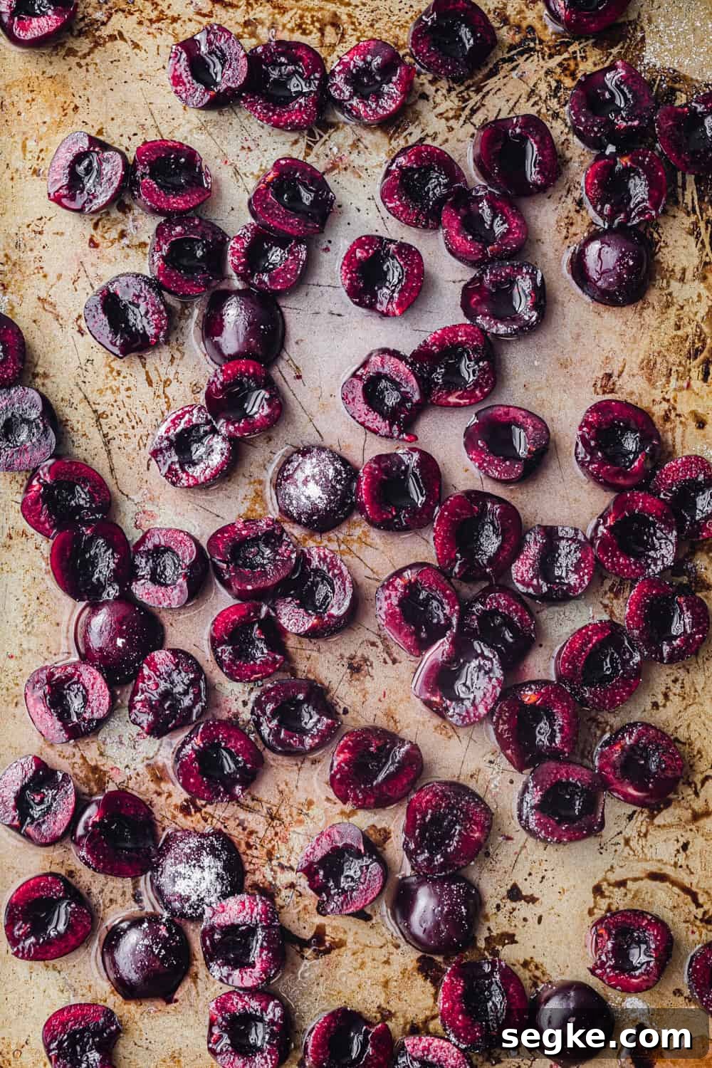 In process shot of raw fresh cherries sprinkled with sugar on gold baking sheet, overhead shot.