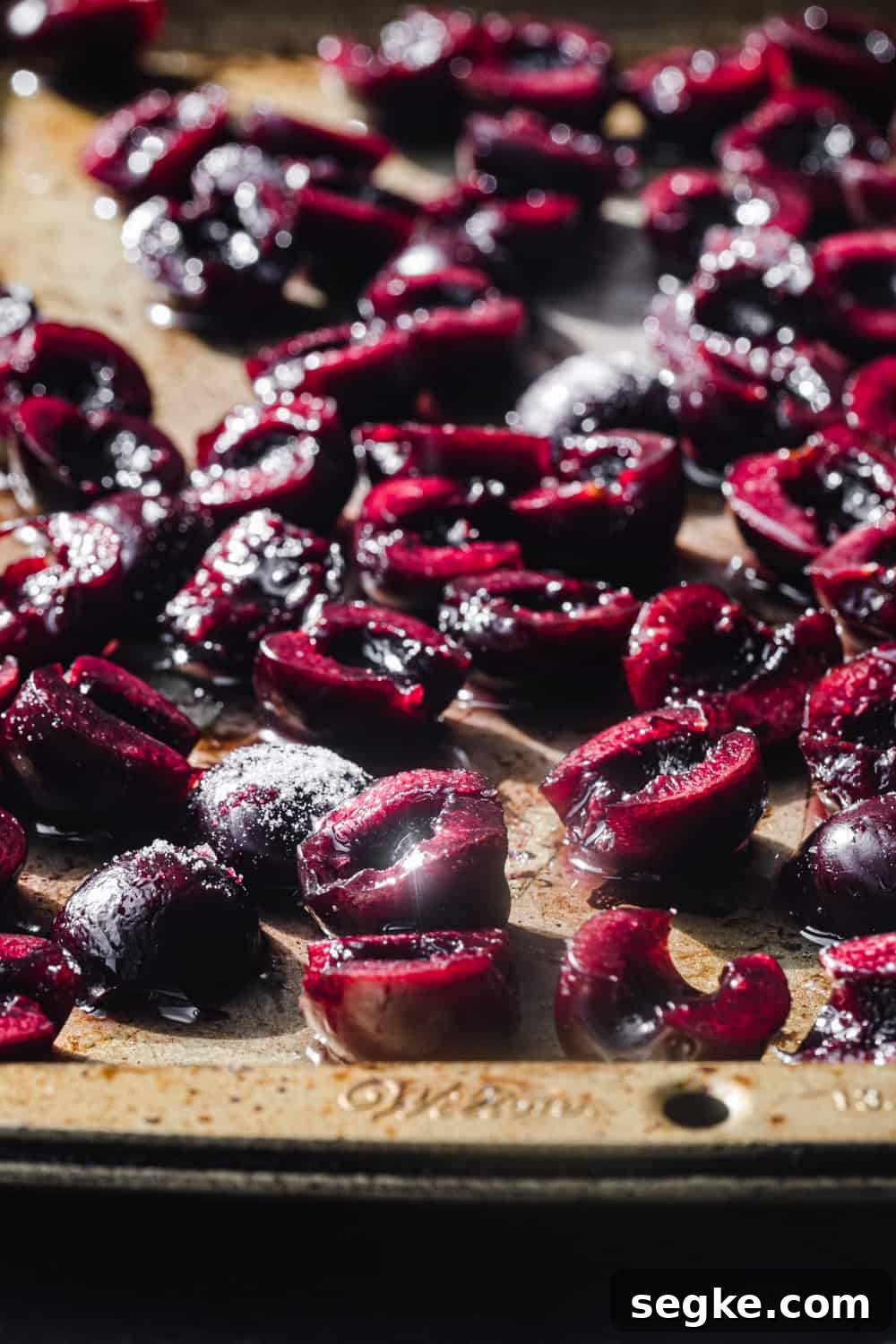 Side angle shot of raw cherries with sugar on a gold baking sheet, all ready to go in the oven and be roasted.