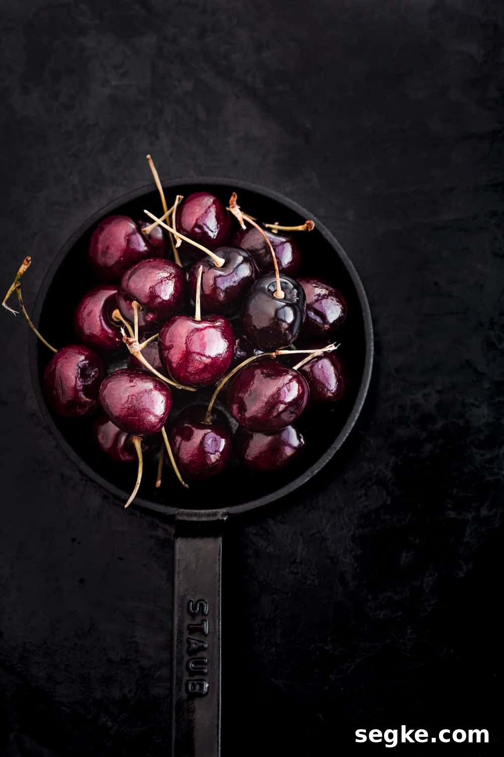 Whole cherries, with their stems, on a little cast iron skillet.