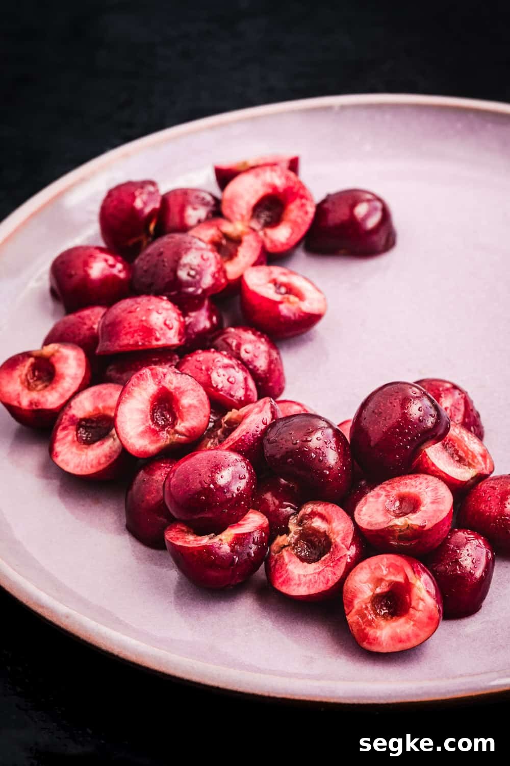 Pitted cherries, cut in half, on a pink plate, side angle shot.
