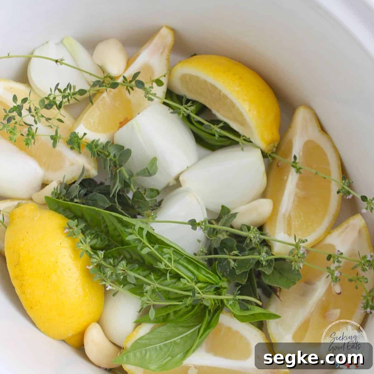 Lemons onions garlic and fresh herbs placed in the bottom of the pot for making slow cooker turkey breast.