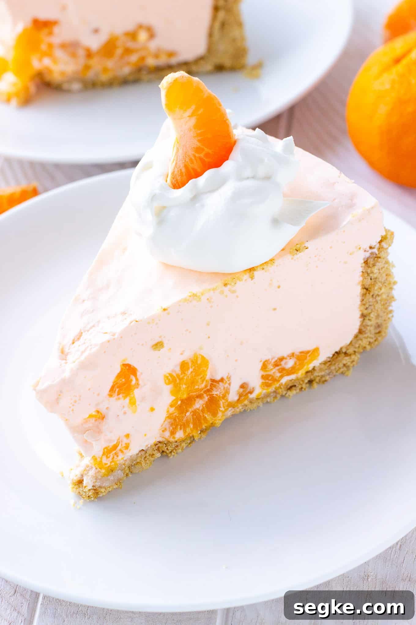 A slice of orange creamsicle pie on a plate topped with whipped cream and a mandarin orange.