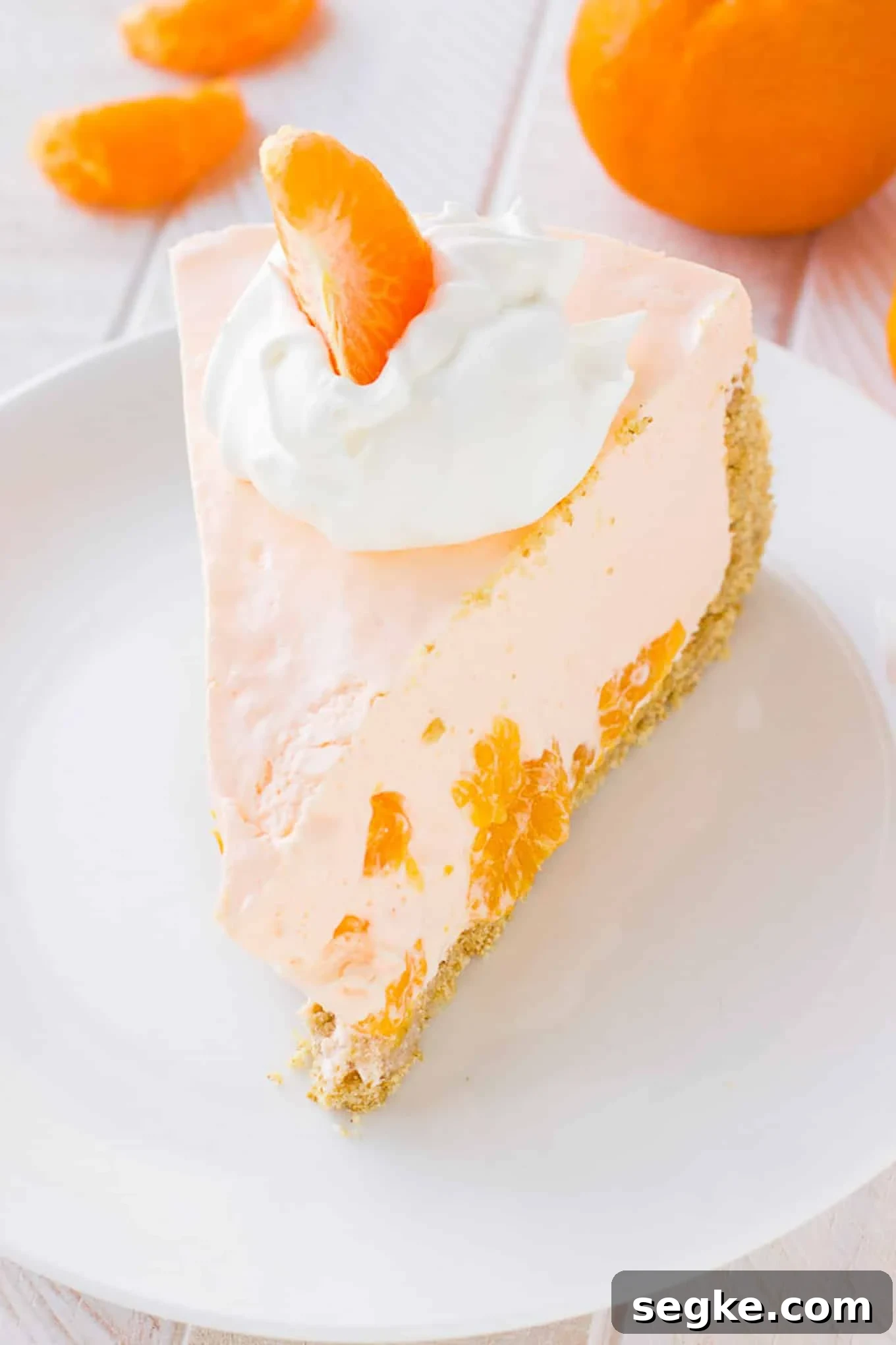 A slice of no-bake orange pie on a plate with some whipped cream and an orange slice.