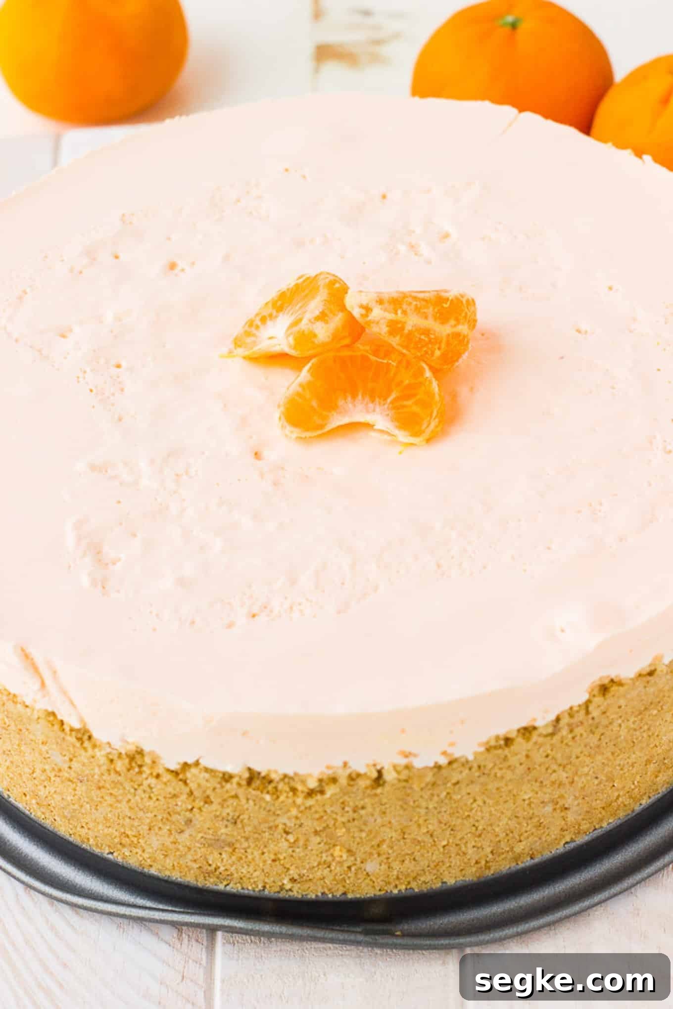 Uncut orange pie out of the cheesecake pan and topped with three mandarin orange segments.