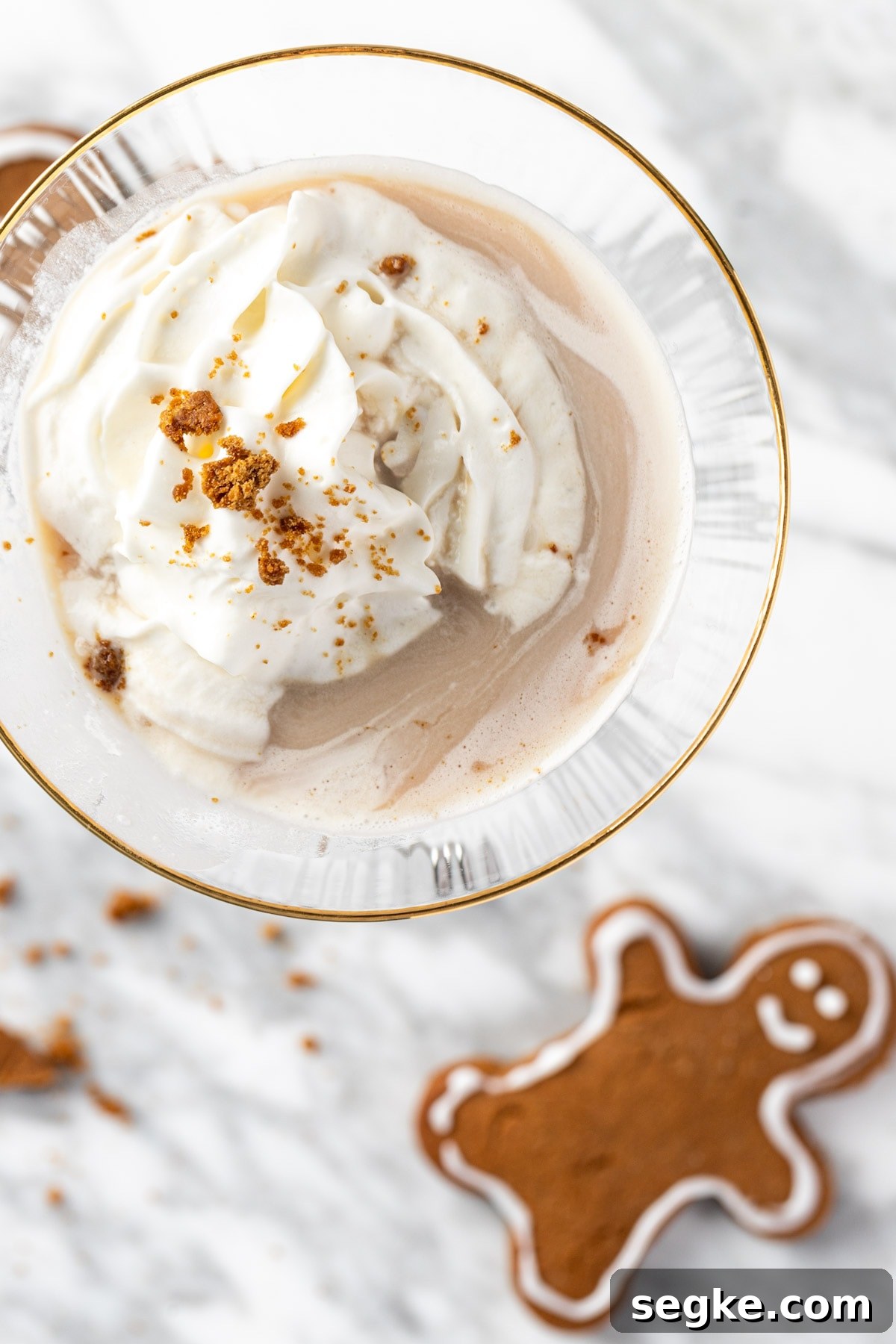 A gingerbread martini on a white marble table next to gingerbread man cookies.